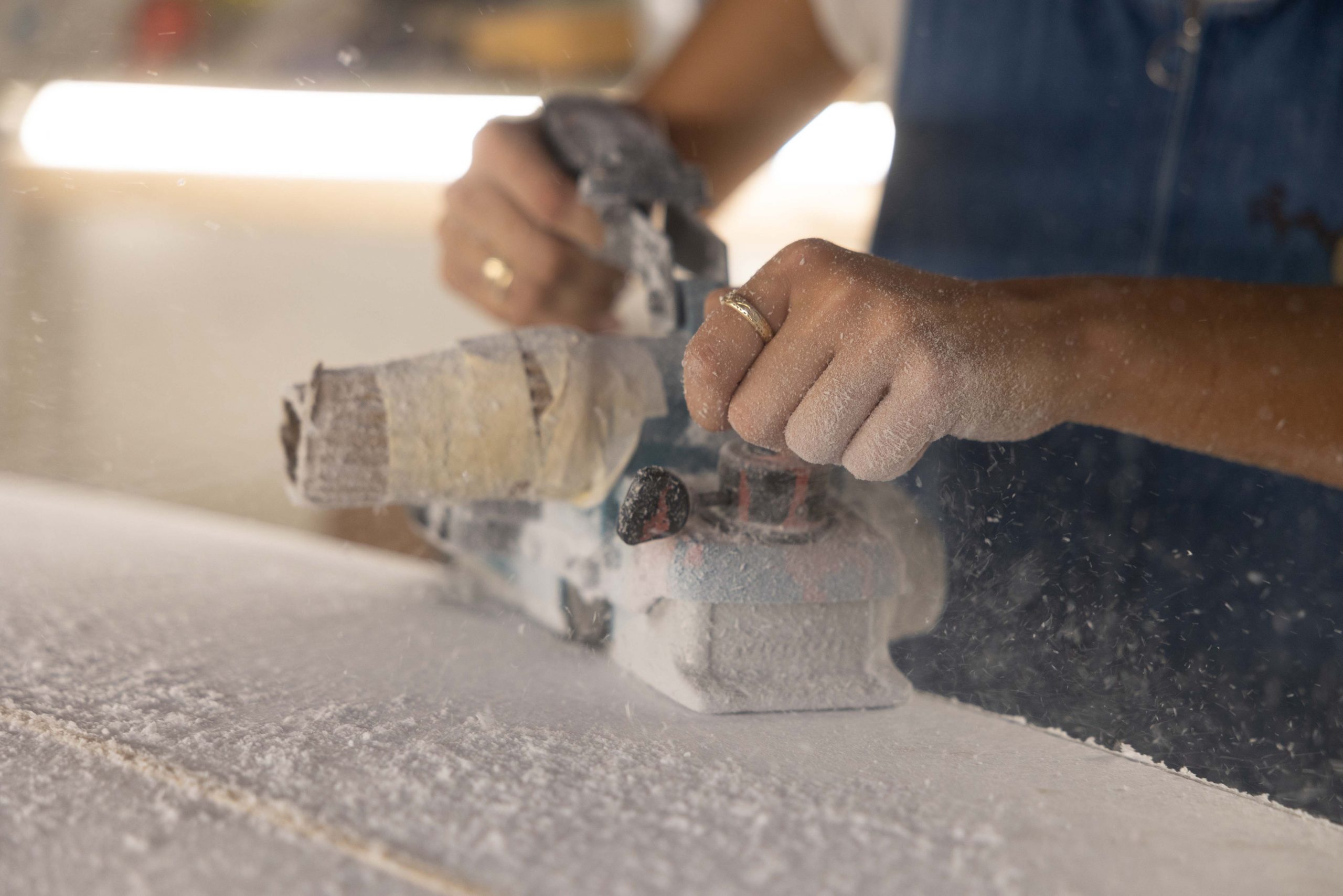 Catherine Girard uses an electric sander to shape a surfboard