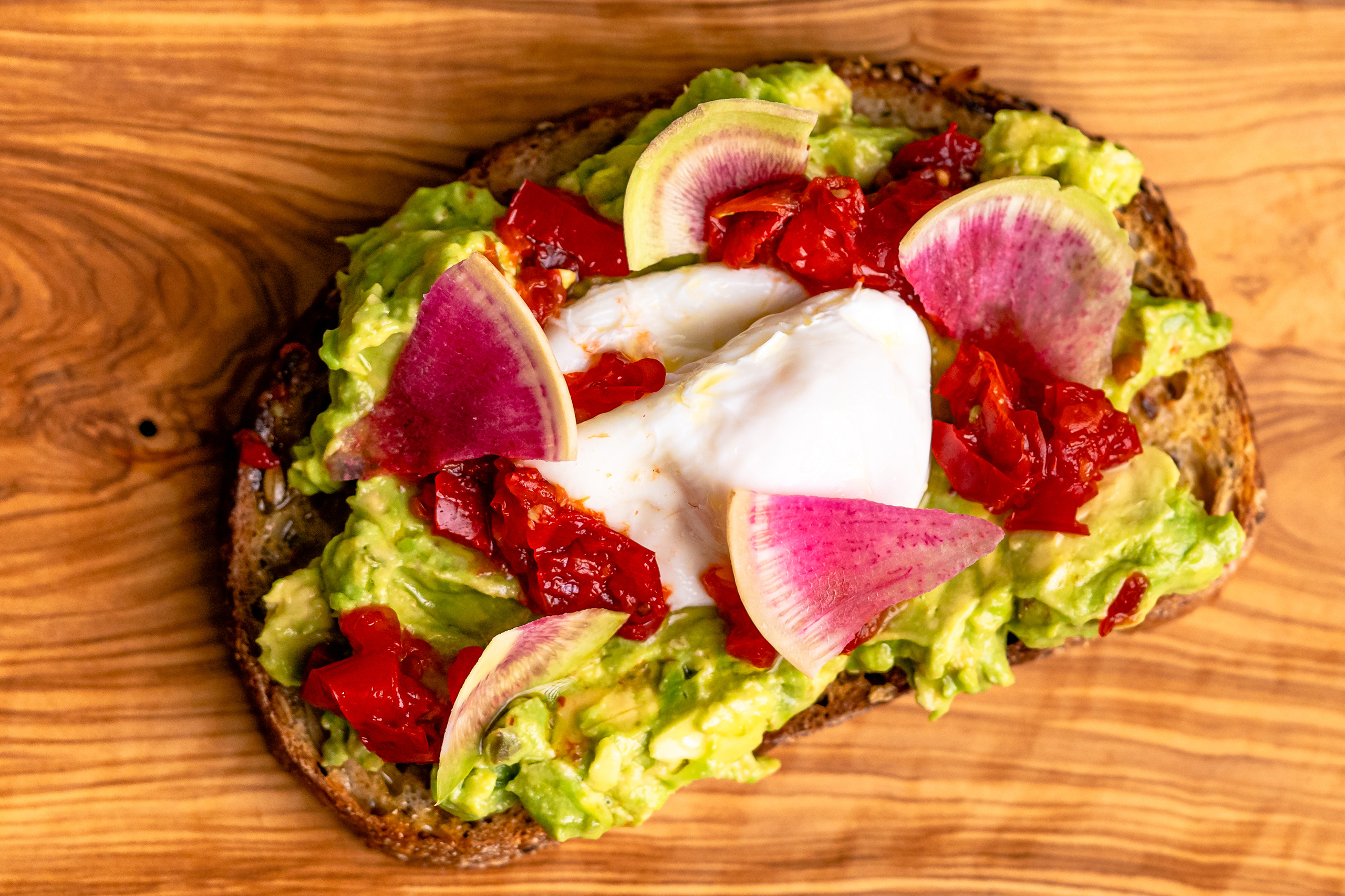 Aerial view of avocado toast with medjool dates, placed on a wooden surface.
