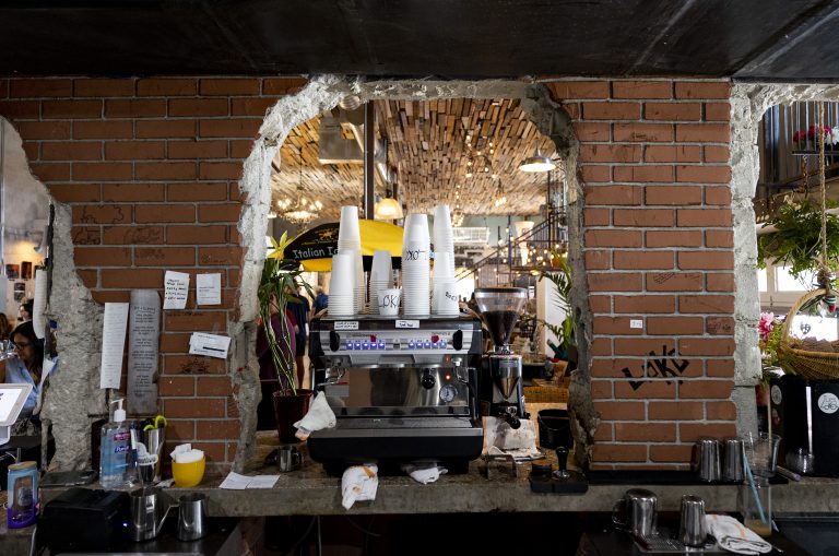 Straight on shot of the espresso machine at the Lokomotive in Jupiter, FL. The machine is stacked with white coffee cups and surrounded by an exposed brick wall.