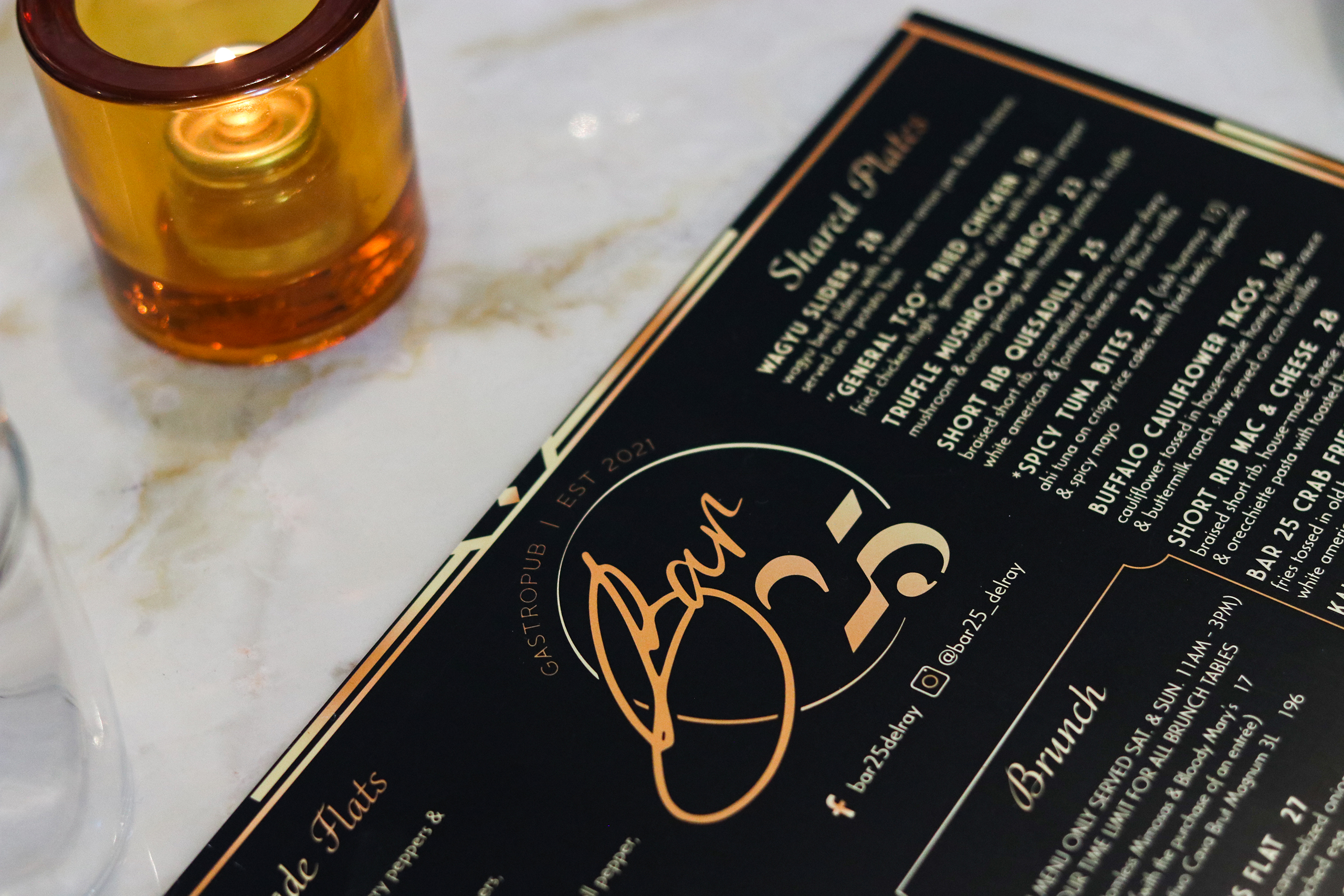 Bar 25 menu, in Delray Beach, FL, placed on marble countertop beside a candle.