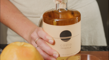 Costa Tequila bottle being opened with two hands. A grapefruit and glass of juice out of focus in the foreground.
