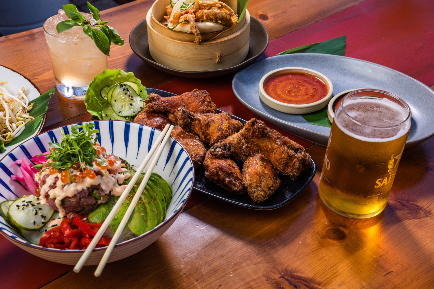 An arrangement of various dishes from Kapow! in Boca Raton, FL. Poke bowl, fried chicken, a pint of beer.