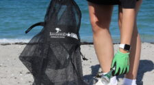 Person bent over picking up a aluminum can to put in her mesh trash bag. Part of a beach cleanup effort in Palm beach County by Loggerhead Marinelife Center.