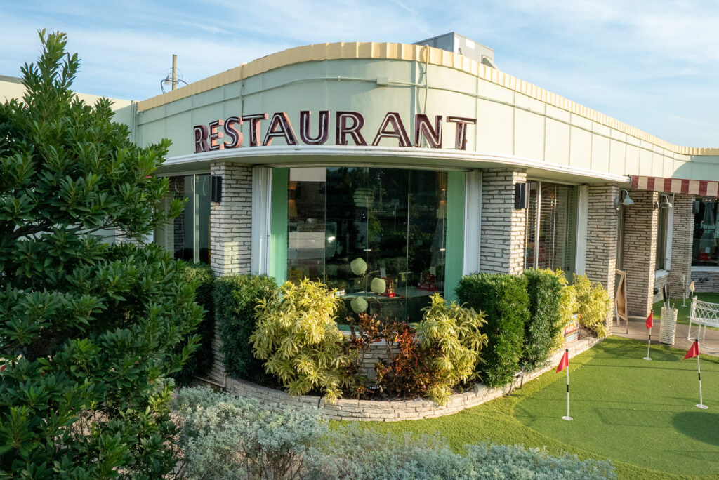 Howley's in West Palm Beach, Florida. Taken from the front corner of the restaurant, the photo shows the greenery that surrounds the retro building, along with the mini golf green located outside. 