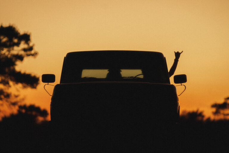 Sunset photo by Brian Hall of a hand throwing up a shaka outside of a truck.