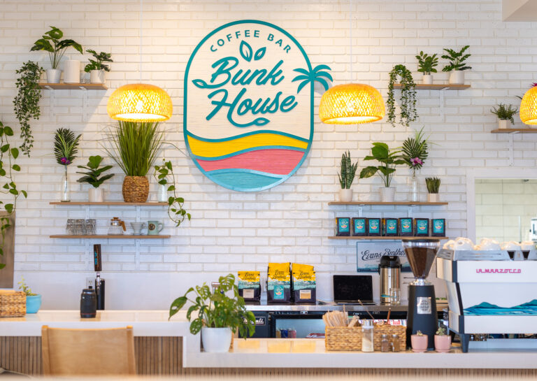 The front counter area of Bunk House, with the white Subway-tiled wall in the background decorated with the store's logo and various plants.