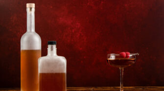 Photos from J.M. Hirsch's new book, freezer door cocktails. Two frosted glass bottles in front of maroon background with a cocktail to the right.