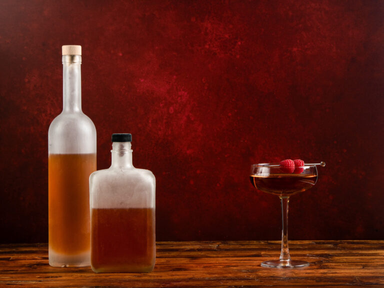 Photos from J.M. Hirsch's new book, freezer door cocktails. Two frosted glass bottles in front of maroon background with a cocktail to the right.