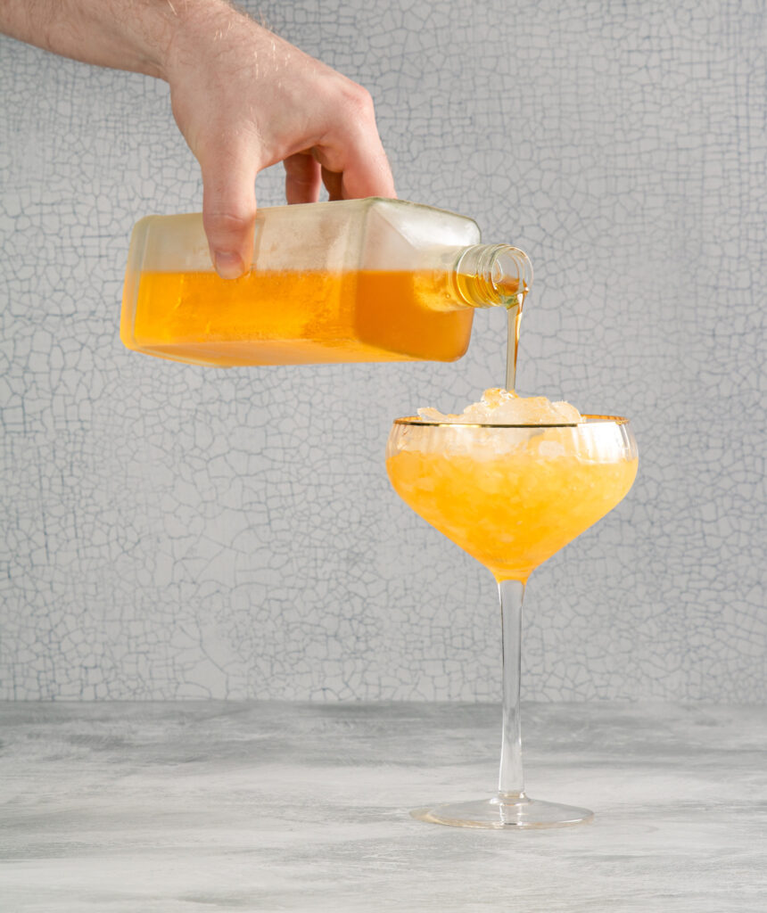 Photos from J.M. Hirsch's new book, freezer door cocktails. Hand pouring yellow lemon drop cocktail into coupe glass.