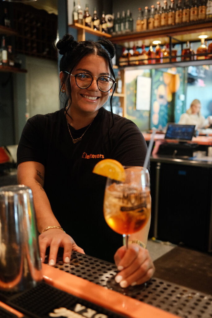 Valeria Ruiz, bartender at Leftover's in Jupiter, passing a cocktail in a wineglass across the bar.