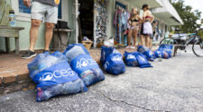 Blueline monthly Paddle Cleanup in Jupiter. Low angle of 4ocean trash collection bags outside of Blueline surf shop. People are visible in the distance, but out of focus.