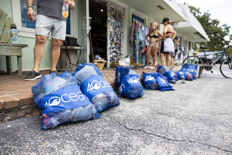 Blueline monthly Paddle Cleanup in Jupiter. Low angle of 4ocean trash collection bags outside of Blueline surf shop. People are visible in the distance, but out of focus.