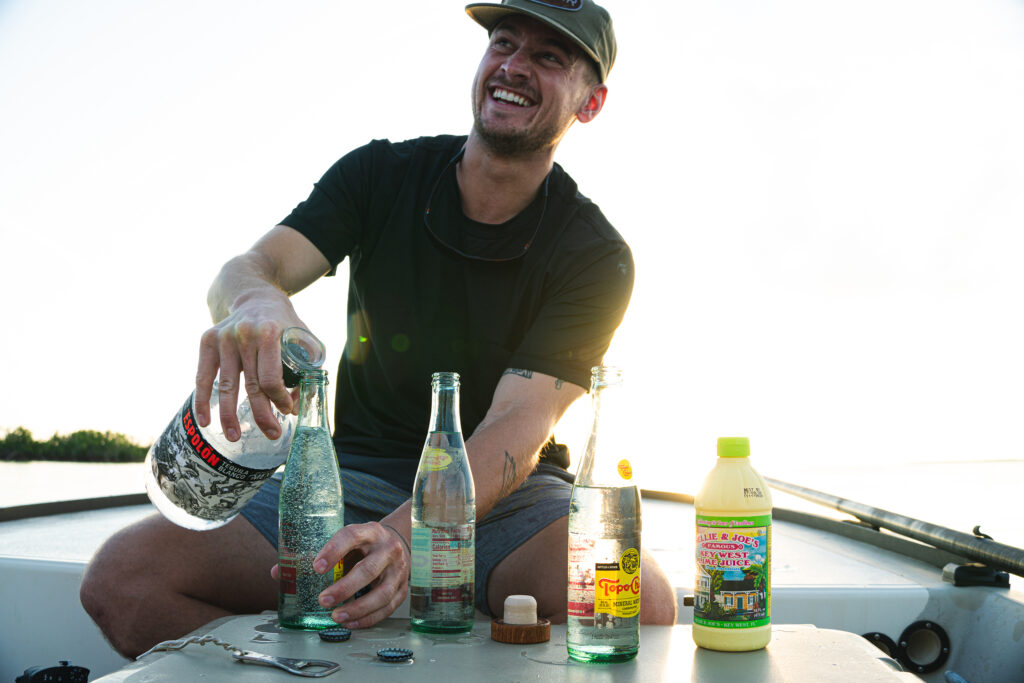 A man pours Espolon tequila into a Topo Chico on a boat. The sun illuminated the frame from behind him. 