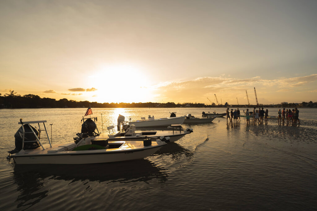 Boats anchored on a sandbar with the sun going down behind them/ 