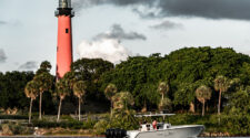 A boat cruising in front of the red Jupiter Lighthouse.