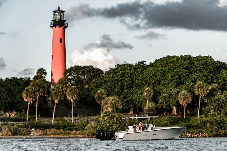 A boat cruising in front of the red Jupiter Lighthouse.
