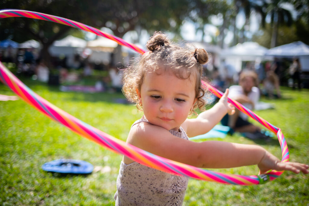 Young girl at Coco Market in Delray Beach swinging a pink hula hoop.