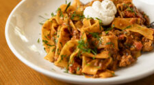 Chef Suzanne Perrotto of Brule Bistro favorite pasta dish. Bolognese on a white plate with a dollop of cream on top and garnished with herbs.