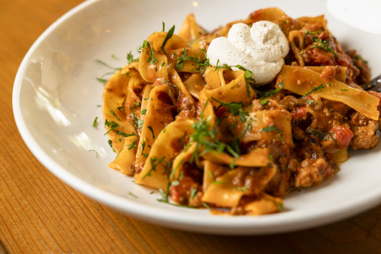 Chef Suzanne Perrotto of Brule Bistro favorite pasta dish. Bolognese on a white plate with a dollop of cream on top and garnished with herbs.