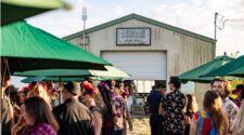 Swank Table Dinner. A crowd of people dressed in Dia De Los Muertos garb and slightly out of focus frame the foreground of SWank Specialty Produce's farmhouse entrance.