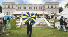 Nick Mele photo. A man with a striped umbrella is walking out of a sprawling estate.