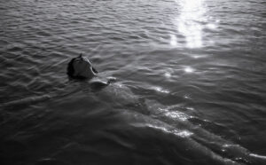 Black and white image of a woman floating on her back in the ocean with the light rippling around her.