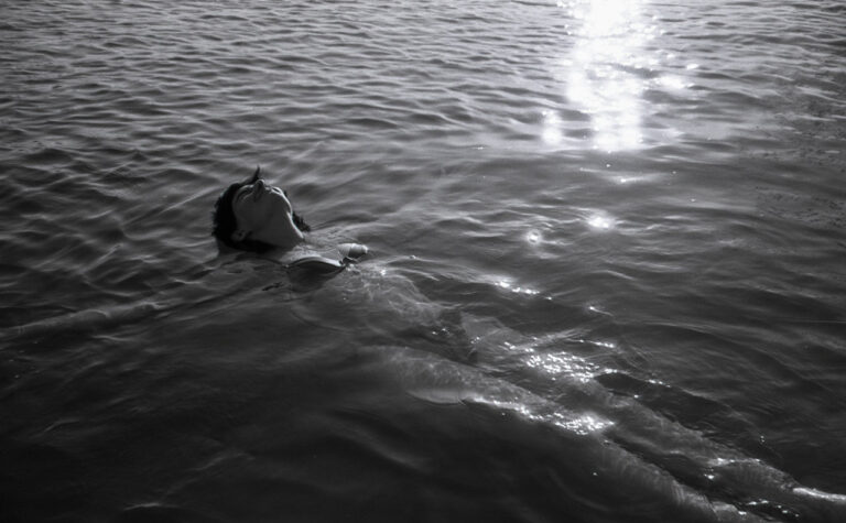 Black and white image of a woman floating on her back in the ocean with the light rippling around her.