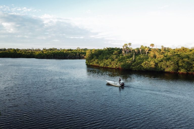 A man guides his single motor boat down the river in Jonathan Dickinson State Park, shaded by clouds and mangroves.
