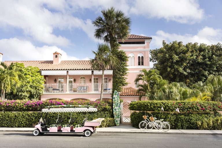 The signature pink tower of the Colony in Palm Beach with a three-row golf cart and two bicycles in front.
