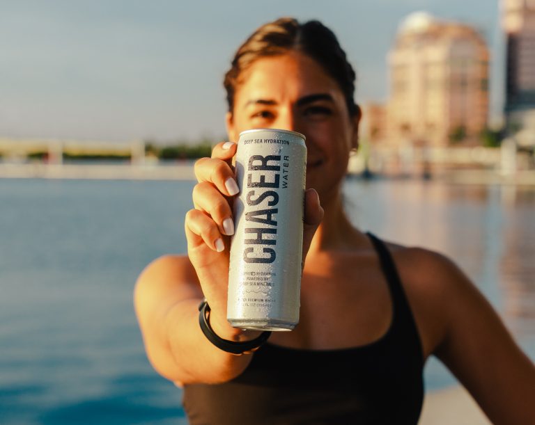 A girl holding a can of Chaser Water out to the camera, with only the can in focus.
