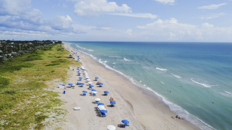 Drone shot of Delray Beach with blue umbrellas lining the sand