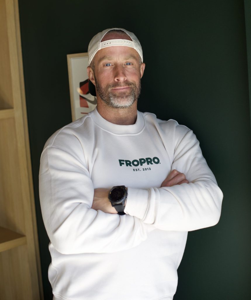 Founder of FROPRO Matt Williams poses for a photo crossing his arms and wearing a white crewneck with FROPRO written across in green letters.