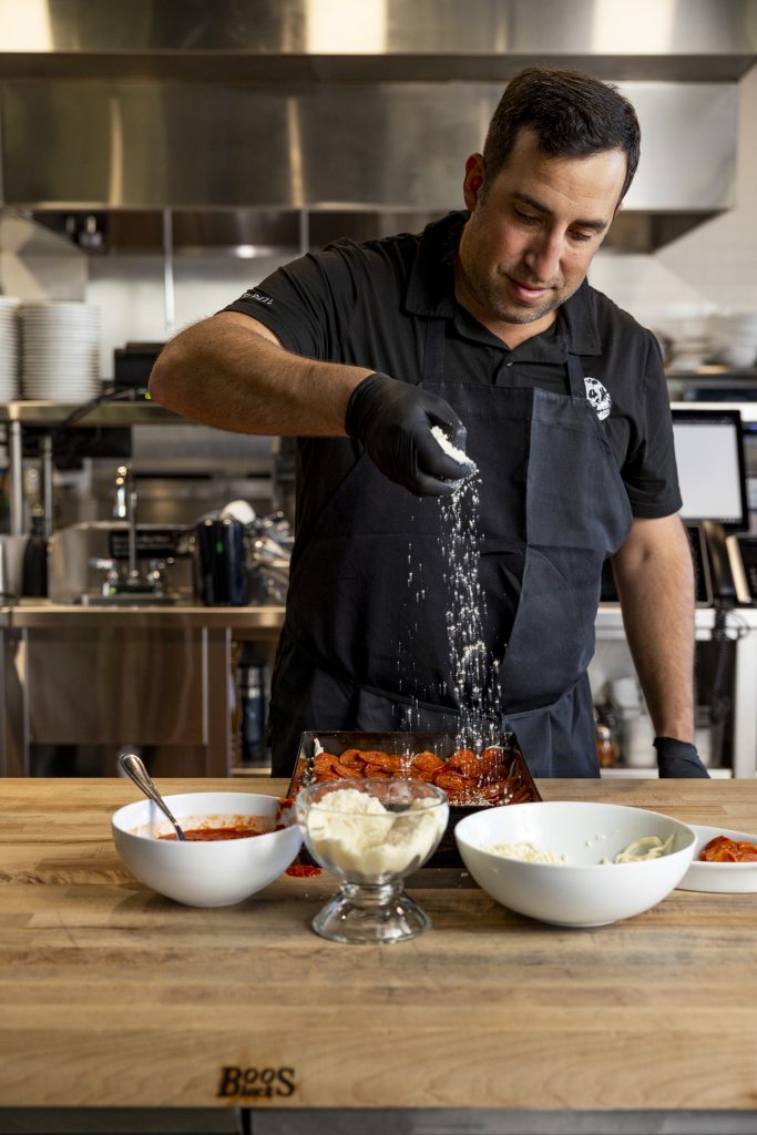 Chef Koby sprinkling Pecorino cheese on a pizza.