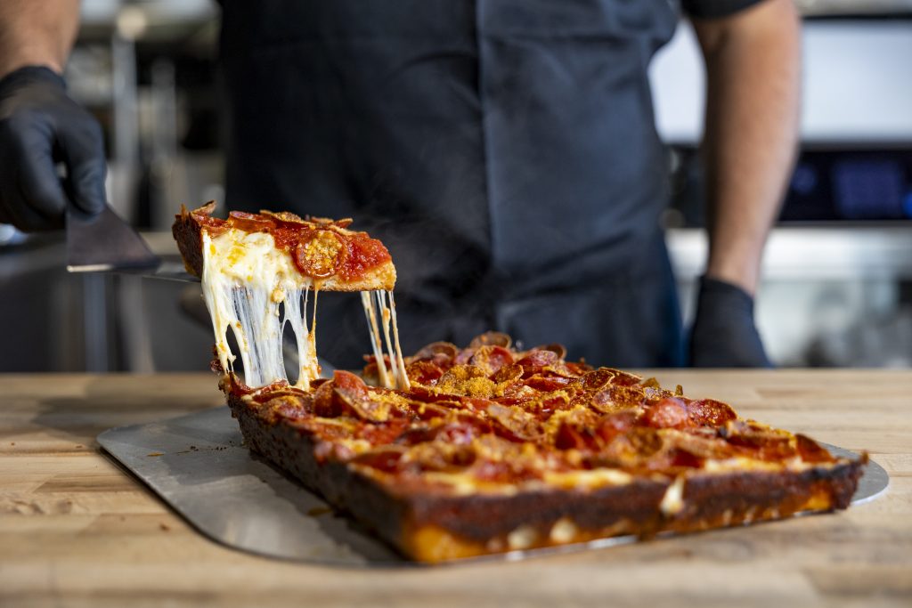 A slice of pizza being pulled away from the whole pie.